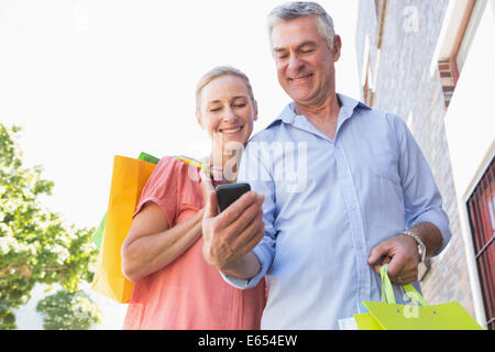Happy senior couple looking at smartphone holding shopping bags Stock Photo