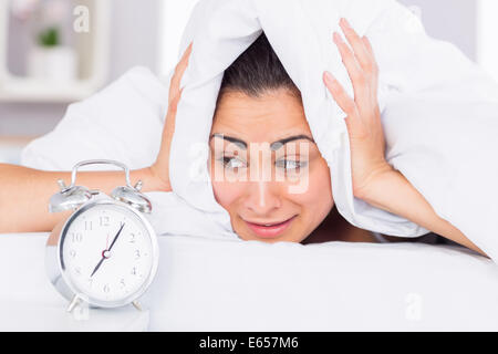 Woman covering ears with sheet in bed Stock Photo