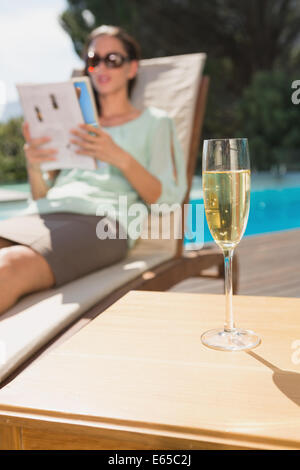 Woman reading book by pool with champagne in foreground Stock Photo