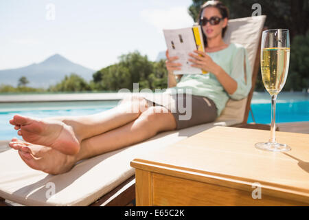 Woman reading book by pool with champagne in foreground Stock Photo