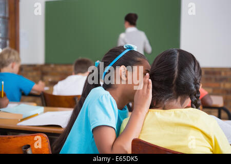 Cute pupils whispering in classroom Stock Photo