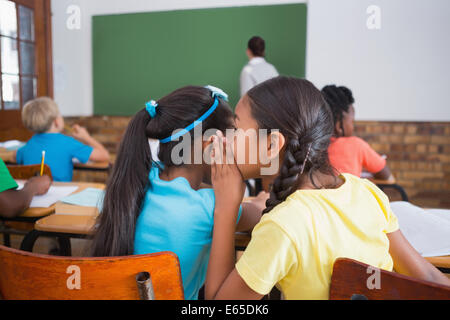 Cute pupils whispering in classroom Stock Photo