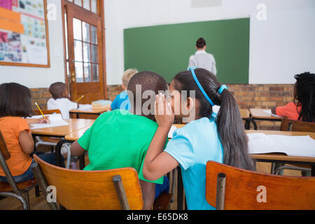 Cute pupils whispering in classroom Stock Photo