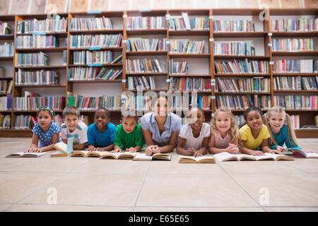 Cute pupils and teacher lying on floor in library Stock Photo