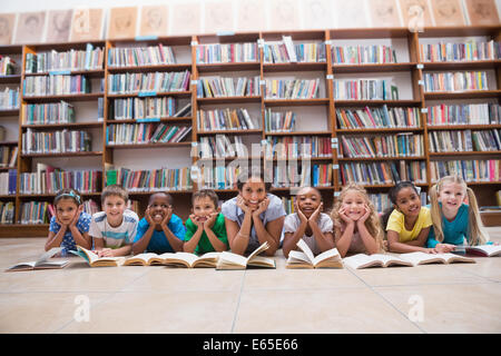 Cute pupils and teacher lying on floor in library Stock Photo