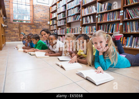 Cute pupils and teacher lying on floor in library Stock Photo