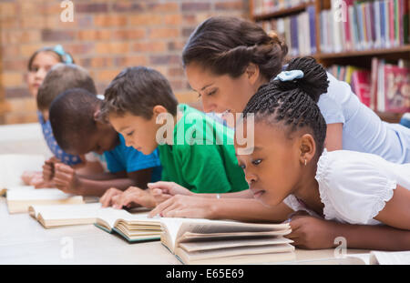 Cute pupils and teacher lying on floor in library Stock Photo