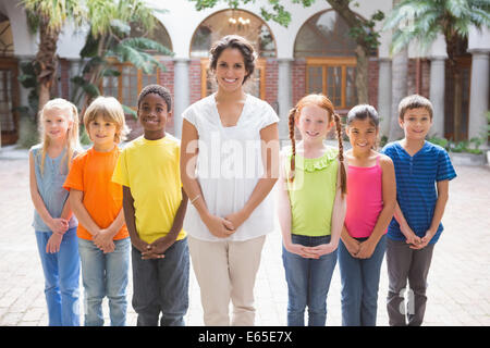 Pretty teacher standing with pupils in courtyard Stock Photo