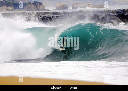 A local surfer pulls into a heavy, shore breaking barrel in shallow water at the surf break The Wedge, in Newport Beach, CA Stock Photo