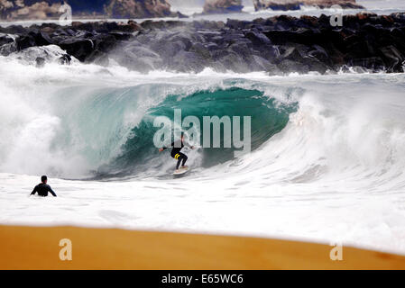 A local surfer pulls into a heavy, shore breaking barrel in shallow water at the surf break The Wedge, in Newport Beach, CA Stock Photo