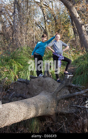 A couple of preteen kids playing on a fallen log. The setting is a forest. Stock Photo