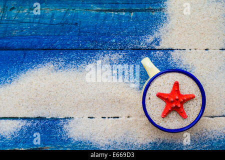 Shell in a cup on the sand strewn on blue boards Stock Photo