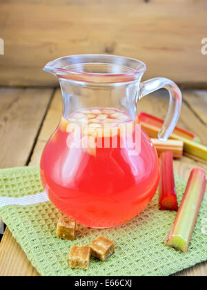 Compote from rhubarb in a jug, sugar, rhubarb stalks on a napkin on the background of wooden boards Stock Photo