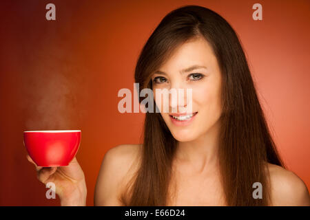 Beautiful young woman with tea pot and mug in her hands over warm background Stock Photo