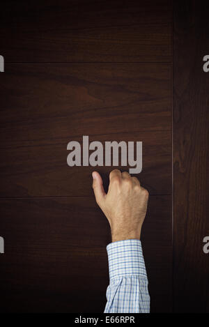 Male hand is knocking on wooden door, conceptual image. Visitor or guest is at the door. Stock Photo