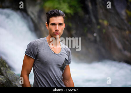 Handsome young man near mountain waterfall looking at camera Stock Photo