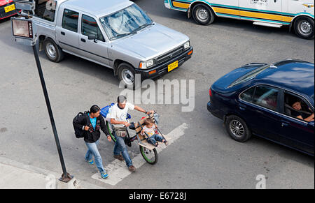 Man wheels bike on road with very young child sitting on homemade wooden seat in front.  Fusagasuga, Colombia, South America. Stock Photo