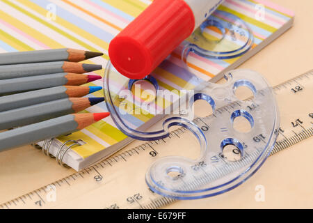 Educational drawing equipment notebook, coloured pencils, glue stick, ruler and geometric shapes stencil on a desktop. England UK Britain Stock Photo