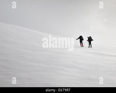 two men with heavy backpacks resting on a snow covered mountain slope in  winter. Huldraheimen, Gausdal Westfjel, Norway Stock Photo