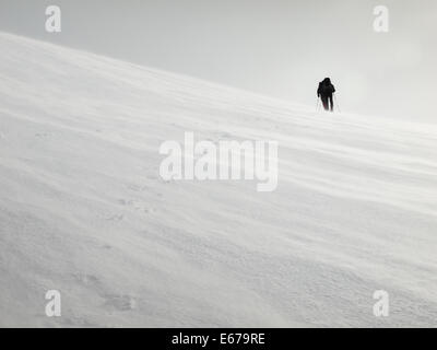 two men with heavy backpacks crossing a snowfield in a storm on snowshoes in  winter mountains with tracks in foreground Stock Photo
