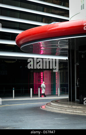 Man in a trench coat walks past the neon red glow of the entrance to the Curve Theatre in Leicester. Stock Photo