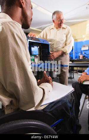 Professor demonstrating furnace electronic control system in HVAC classroom one student in wheelchair Stock Photo