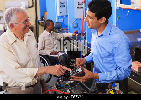 Student examining electrical control system on furnace with professor in HVAC classroom one student in wheelchair Stock Photo