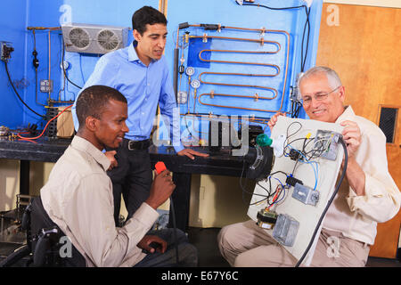 Instructor demonstrating air conditioner control system on demo board to students in HVAC classroom one student in wheelchair Stock Photo