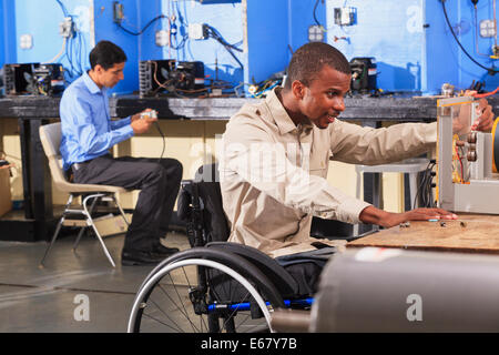 Student in wheelchair setting up generator experiment while student examines HVAC system Stock Photo