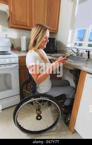 Woman with spinal cord injury in her accessible kitchen using a mobile phone Stock Photo
