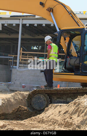 Construction engineer standing on the excavator inspecting the trench Stock Photo