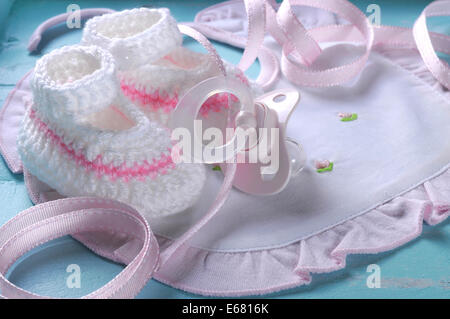 Close up of baby girl nursery dummy pacifier and pink and white wool booties and bonnet on aqua vintage shabby chic background Stock Photo