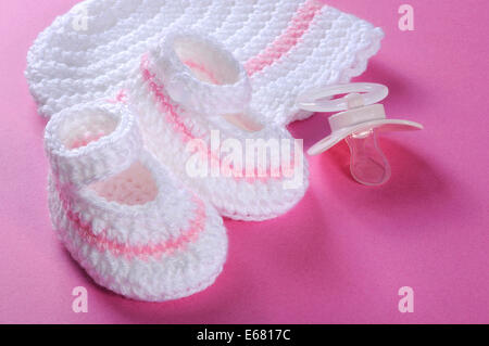 Close up of baby girl nursery pink and white stripe wool booties, bonnet and pacifier dummy on pink background Stock Photo