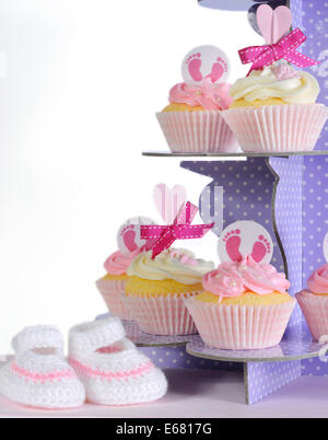 Pink theme baby girl cupcakes and booties on purple polka dot cupcake stand against white background for baby shower or new born Stock Photo