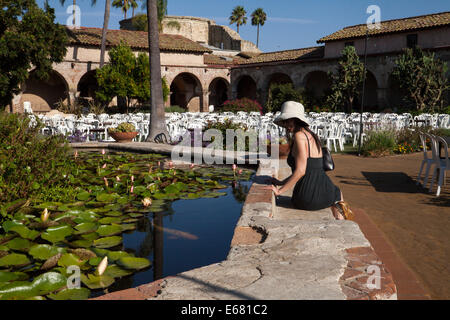 Female Asian watching the carp fish in the lily pond inside the Mission San Juan Capistrano, California, USA Stock Photo