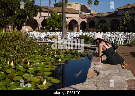Female Asian watching the coy fish in the lily pond inside the Mission San Juan Capistrano, California, USA Stock Photo