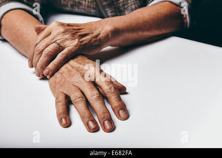 Close-up image of senior woman sitting by a table with focus on her hands. Old female hands on a desk. Stock Photo