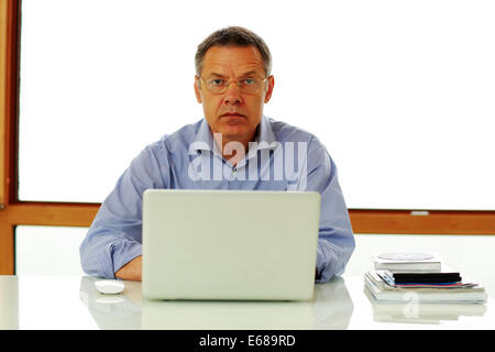 Portrait of a middle aged man sitting on the table with laptop computer. Stock Photo