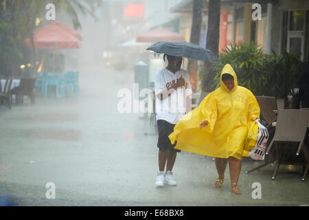 A man holding an umbrella and a woman wearing a rain coat to keep themselves out the rain storm Stock Photo