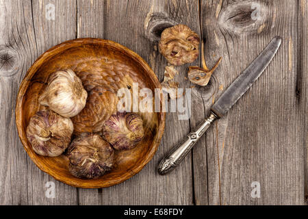 Garlic bulbs lying on a wooden plate and stand on an old rustic wooden table in country style Stock Photo