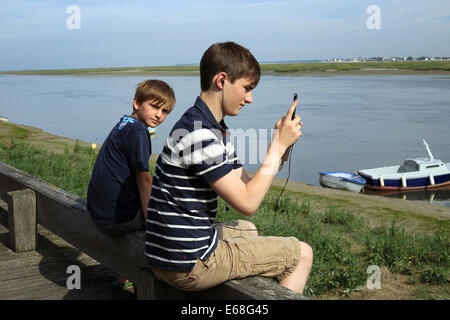 Boys sitting on edge of Quai Blavet, St Valery sur Somme, Somme, Picardy, France. one boy using ipod Stock Photo
