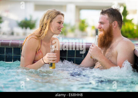 Young woman and a man sitting in hot tub pool with bubbling water while drinking beer. Stock Photo