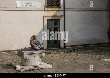 Man sits don the covered well and looks out on the deserted Campo San Marziale in Venice. Stock Photo