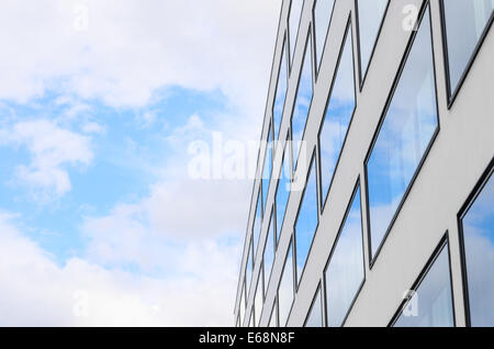 Blue sky and clouds reflected in mirrored windows of new modern building glass facade. Background with free copy-space area for Stock Photo