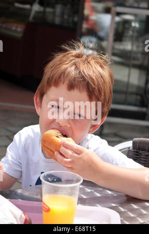 A five year old boy eating a doughnut at La Brioche Doree, France Stock Photo