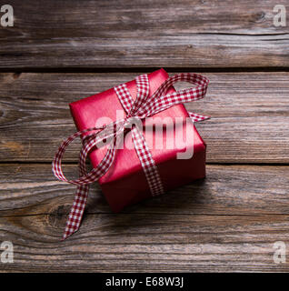 One red christmas present wrapped in red paper with checked ribbon on wooden rustic background. Stock Photo
