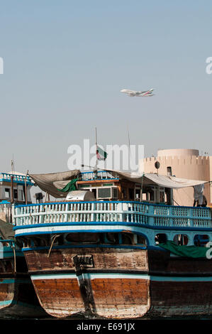 Jet flying over dhows docked moored in Bur Dubai Creek Al Hamriya DIstrict, Dubai, United Arab Emirates UAE. Stock Photo