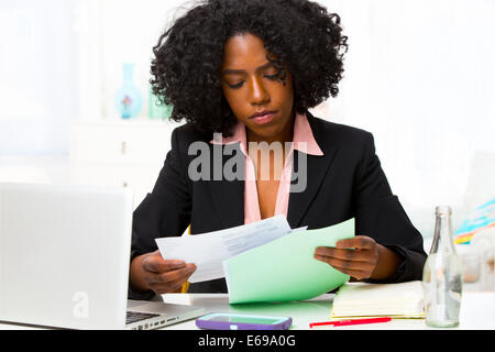 Mixed race businesswoman reading papers at desk Stock Photo