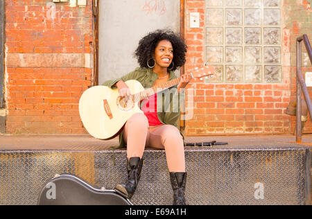 Mixed race woman playing guitar in city Stock Photo