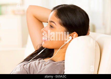 Hispanic woman listening to earphones on sofa Stock Photo